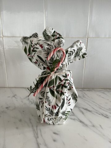 A festive dish towel wrapped around a gift with a candy cane attached to it.